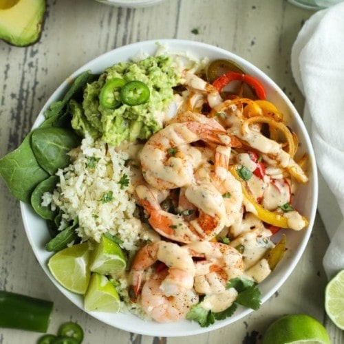 Overhead view of One-Pan Shrimp Fajita Bowls served over cauliflower rice and drizzled with spicy ranch dressing.