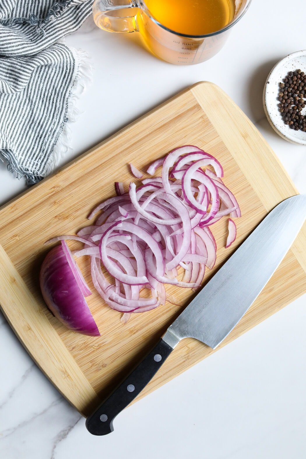 Overhead view of a wooden cutting board with thinly sliced red onions on it with a knife on the side.