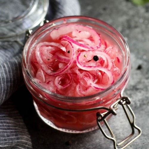 Overhead view of quick pickled onions in a small jar with peppercorns.