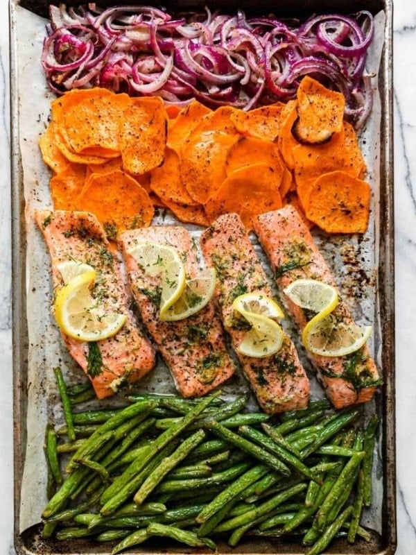 Overhead view of sheet pan filled with salmon fillets, sweet potato rounds, long fresh green beans, and red onions sliced.