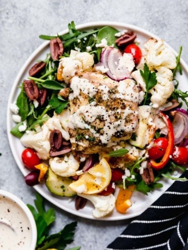 Overhead view of Sheet Pan Mediterranean Chicken and Veggies served over mixed greens and drizzled over tahini lemon dressing.