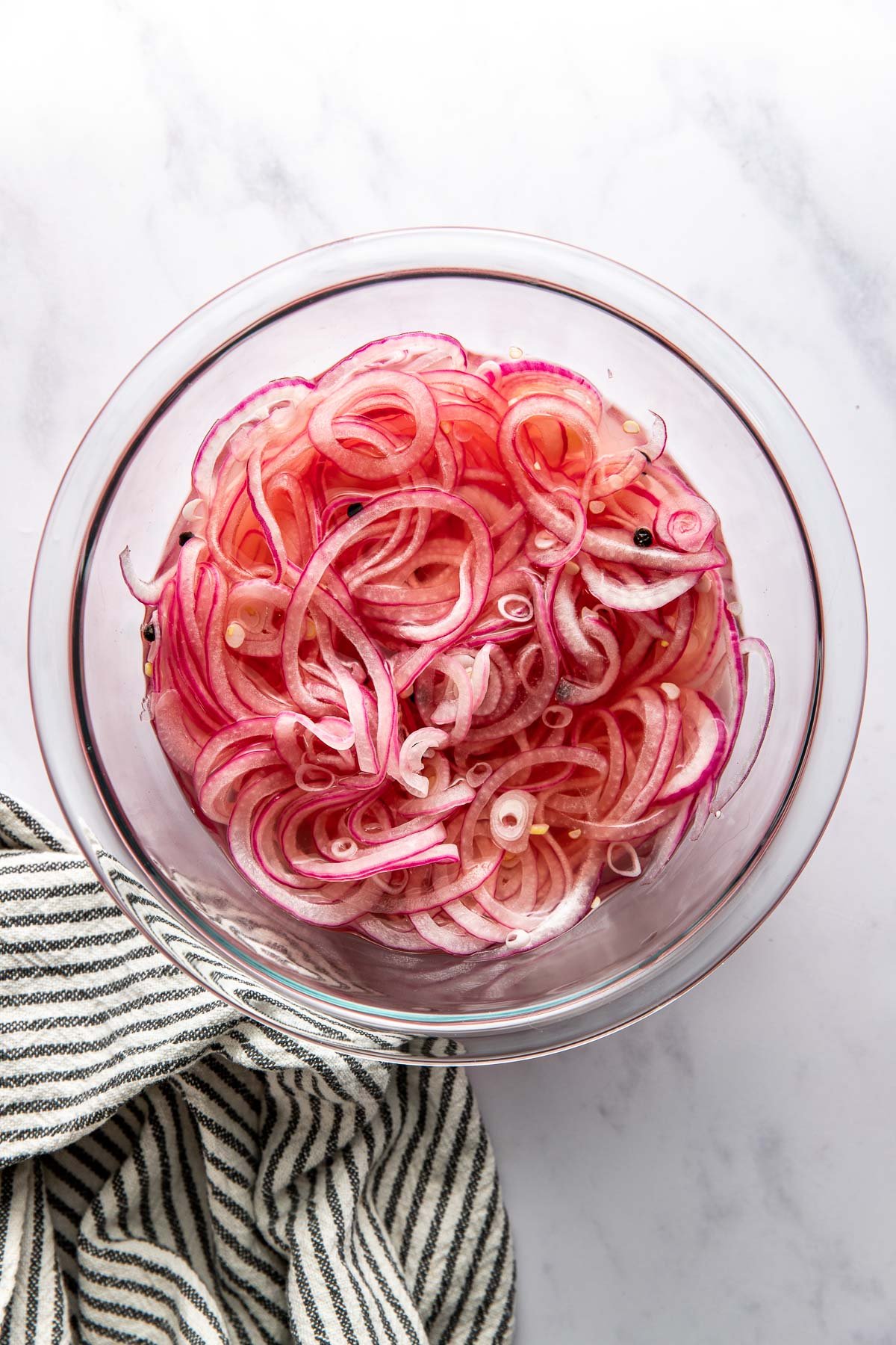 Overhead view of a glass bowl filled with Quick Pickled Onions topped with peppercorns. 