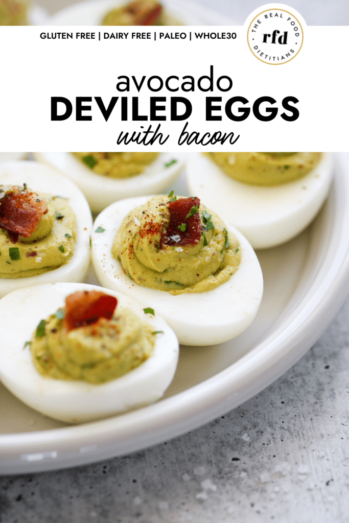Avocado deviled eggs topped with bacon and paprika on a white platter.