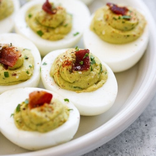 Avocado deviled eggs with creamy avocado filling topped with pieces of bacon.