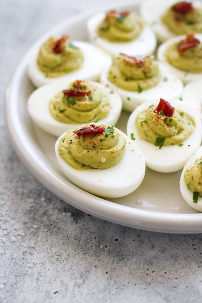 Several avocado deviled eggs with bacon served on white platter