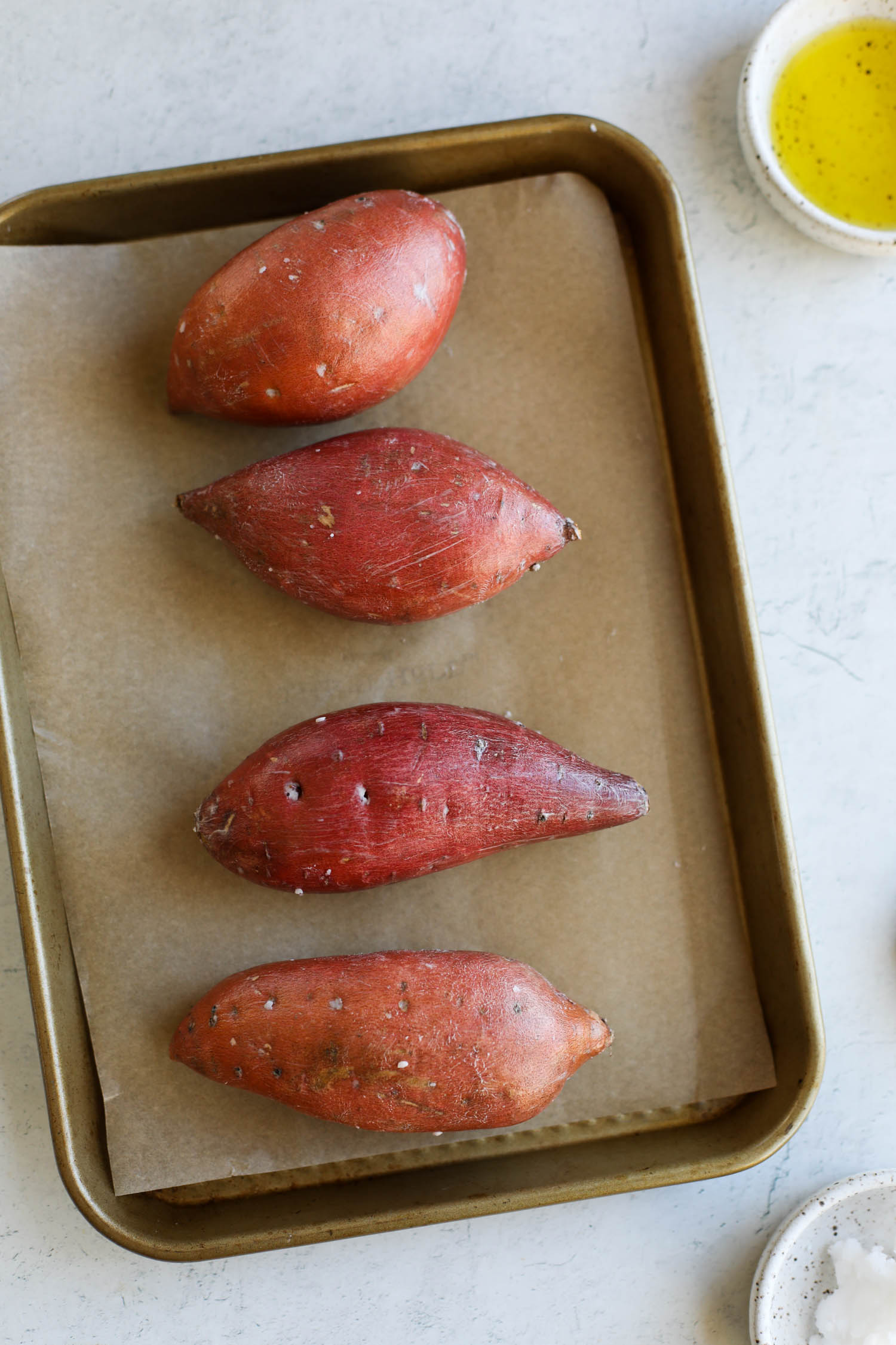 Four sweet potatoes rubbed with oil and flaky sea salt on parchment lined baking sheet.