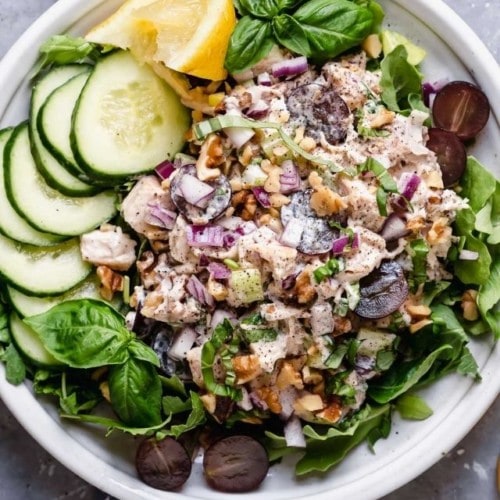 Chicken Waldorf Salad on a white plate over a bed of mixed greens topped with walnuts and fresh herbs.