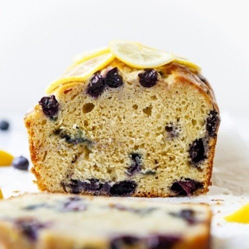 A loaf of Gluten-free Lemon Blueberry Bread with Glaze with a slice cut off to show bread texture.