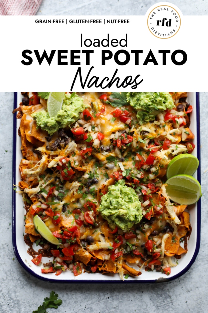Overhead view of loaded sweet potato nachos made with sweet potato chips, shredded chicken, veggies, melted cheddar cheese, and dollops of guacamole.