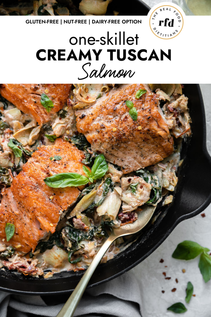 Close up overhead view of creamy Tuscan salmon fillets in a creamy sauce with artichoke hearts, sun-dried tomatoes, basil, and spinach, in a cast iron skillet.