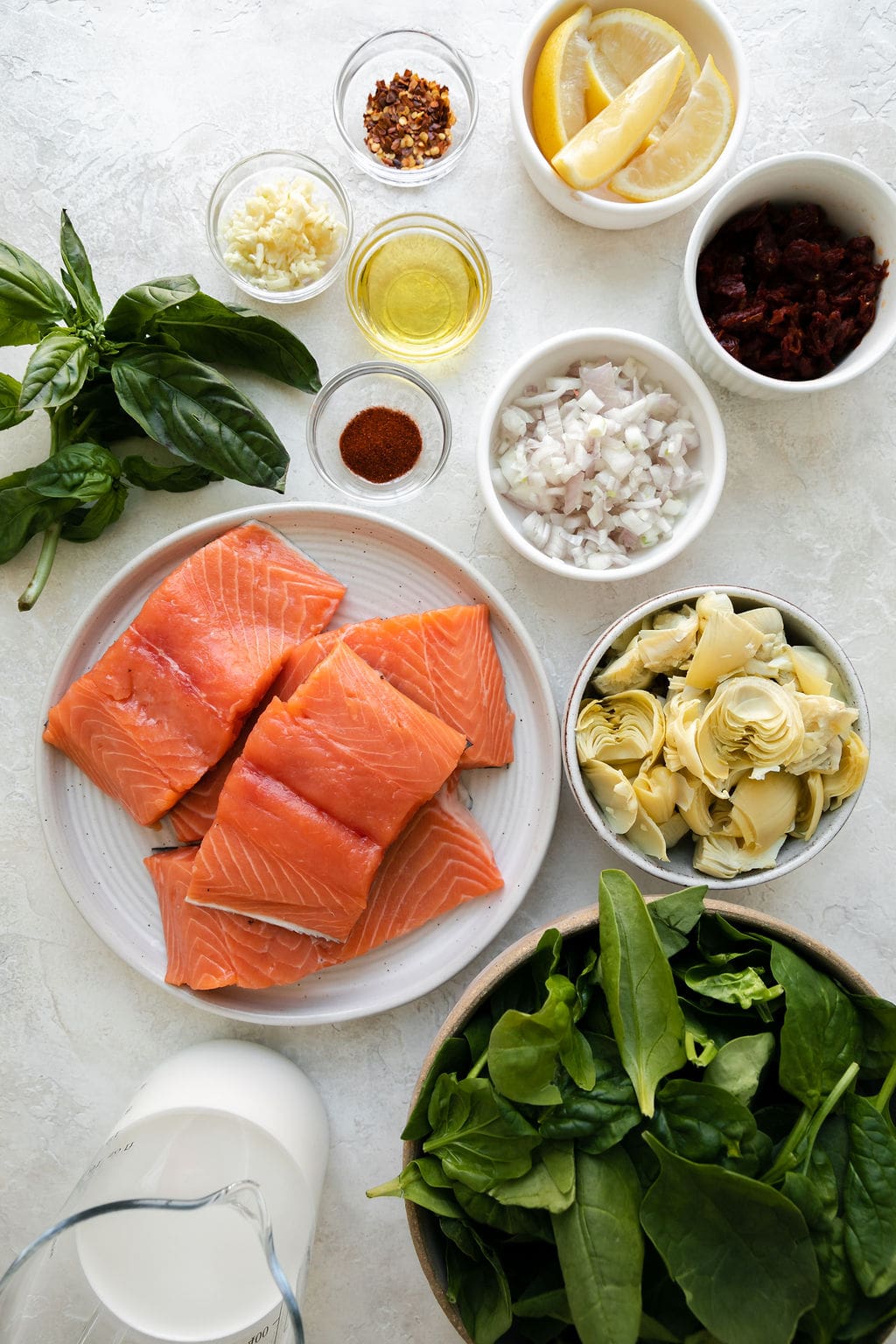 Overhead view of all ingredients for Skillet Creamy Tuscan Salmon arranged together in small bowls and one plate.