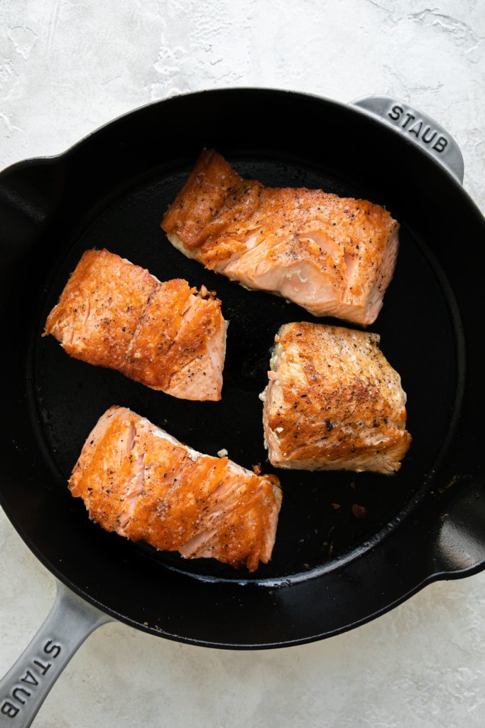 overhead view of four salmon fillers in a cast iron skillet