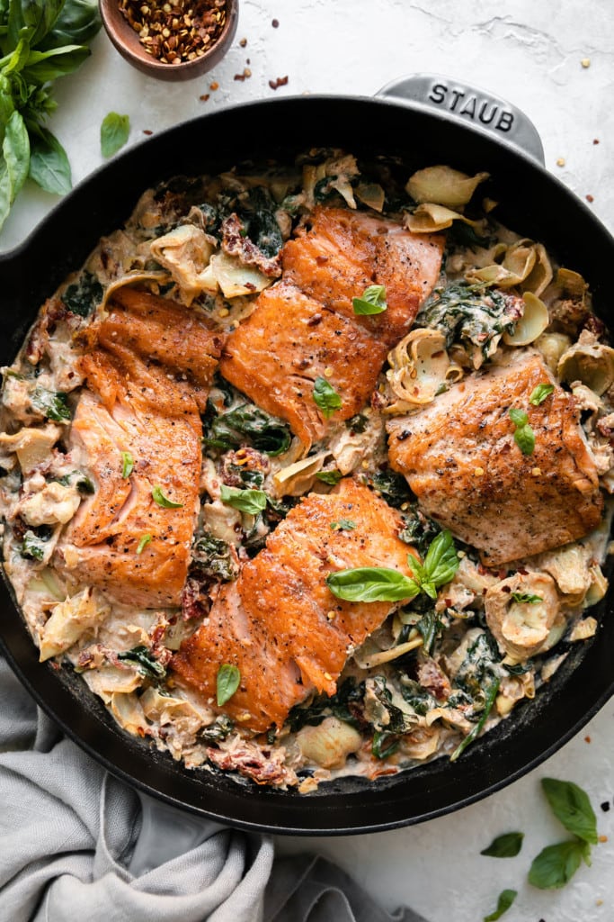 Overhead view of creamy tuscan salmon with artichokes in a cast iron skillet.