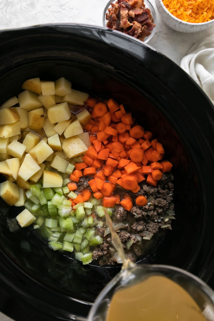 All ingredients for slow cooker cheeseburger soup with bacon in a black crockpot.