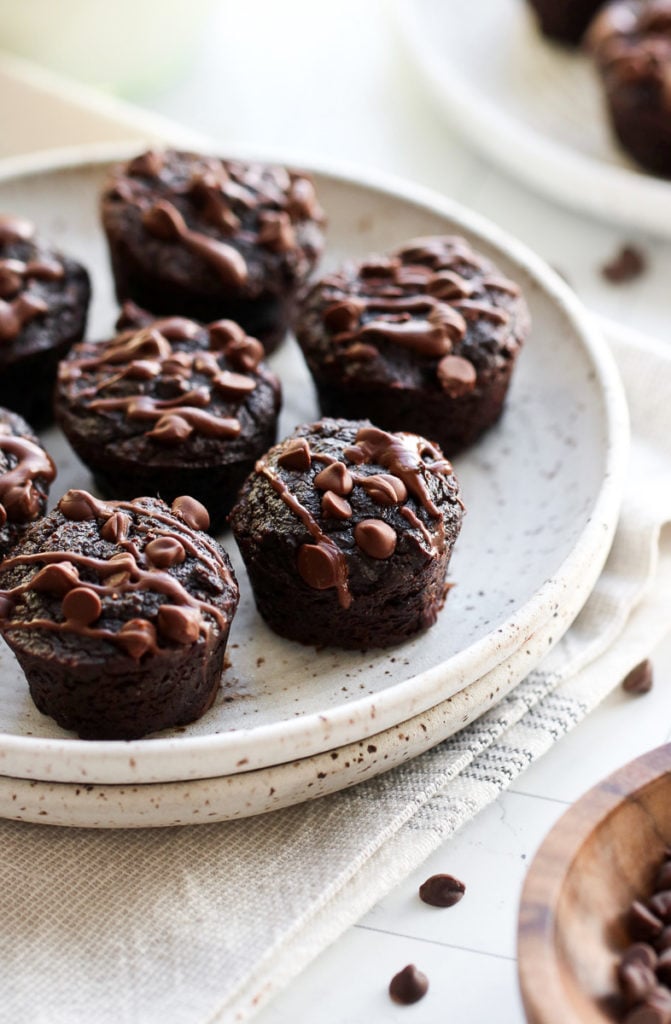 Grain-free sweet potato avocado brownie bites topped with mini chocolate chips and chocolate drizzle on a speckled plate.