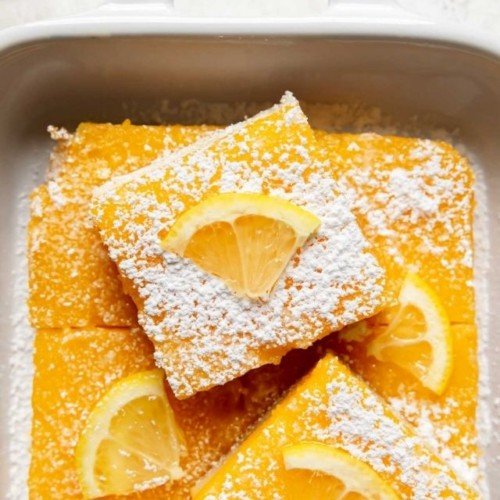 Gluten Free Lemon Bars sprinkled with powdered sugar and lemon slices in a white baking dish.