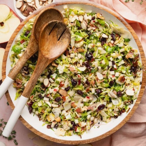 A shaved Brussels sprouts salad in a bowl with two wooden serving spoons on top.