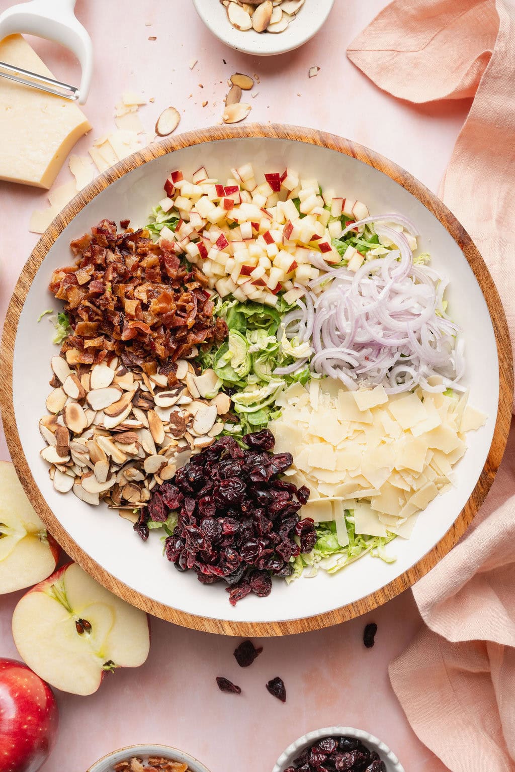 A bowl of shaved Brussels sprouts, Parmesan, raisins, almonds, bacon, apples, and onions.