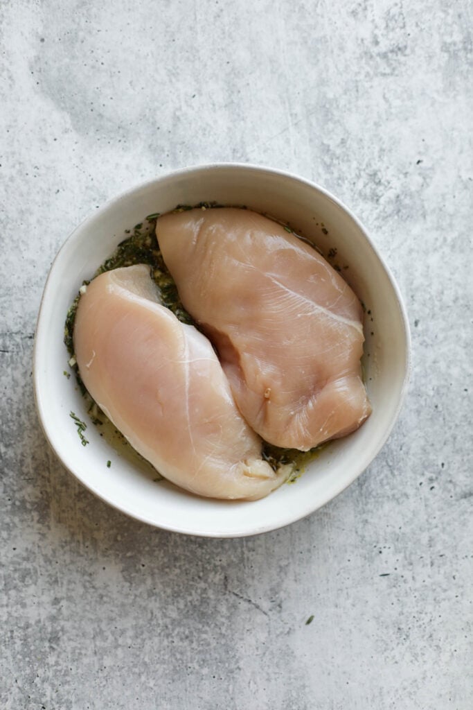 Overhead view of chicken breasts in a white bowl marinating in lemon herb chicken marinade. 