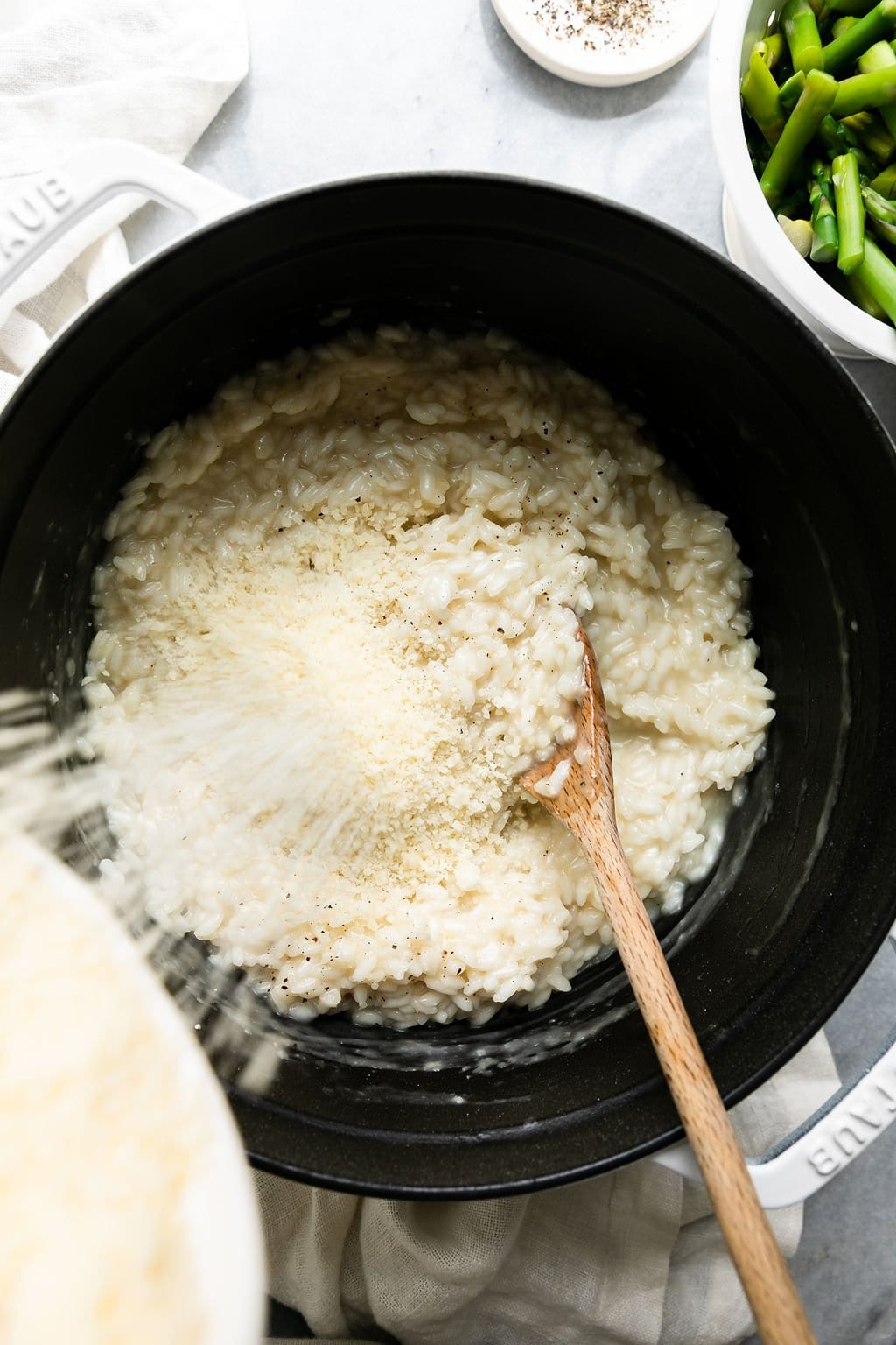 Cheese being poured into cooked rice in a white dutch oven for lemon asparagus risotto. 