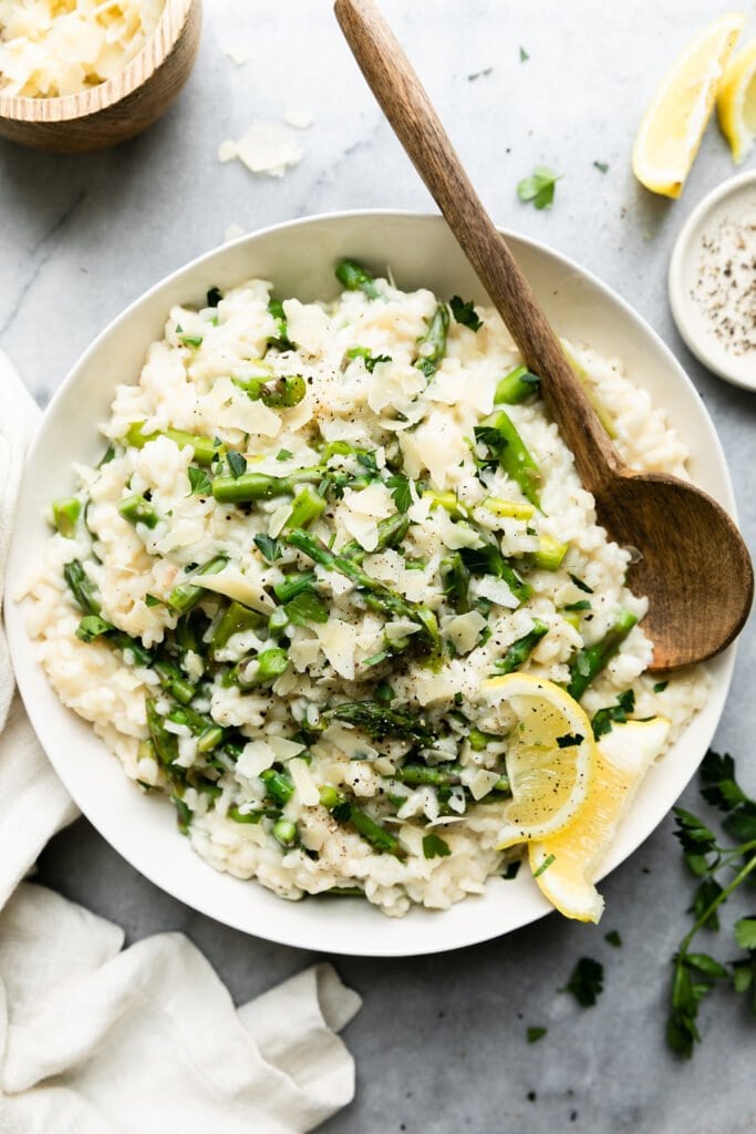 Overhead view of creamy lemon asparagus risotto in a white bowl with a wooden serving spoon on the side. 