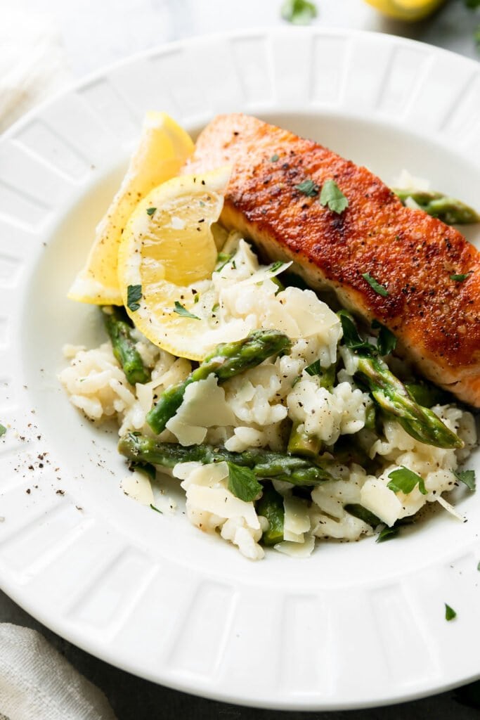 Close up view of creamy lemon asparagus risotto in a white bowl with a salmon fillet on the side. 