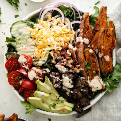 Overhead view of loaded burger bowl in a white bowl drizzled with special sauce.