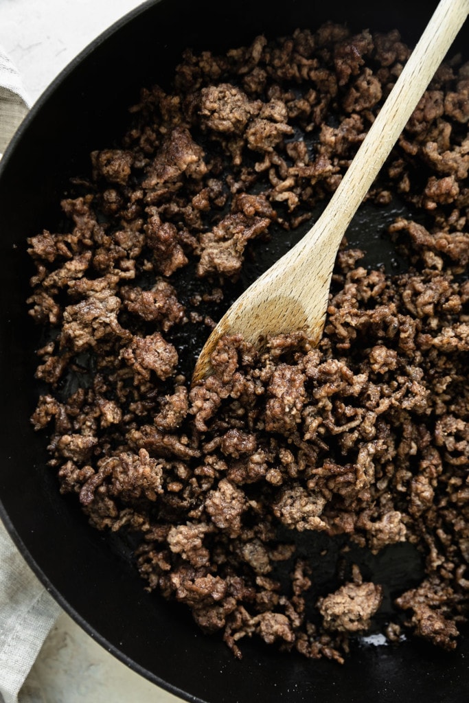 Ground beef in a skillet being stirred with a wooden spoon