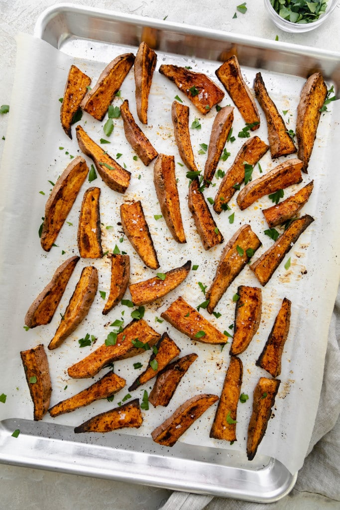 Overhead view of oven baked sweet potato fries on a parchment-covered baking sheet.