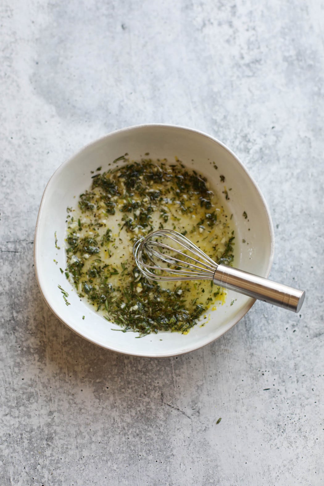 Overhead view of lemon herb chicken marinade in a white bowl with a whisk