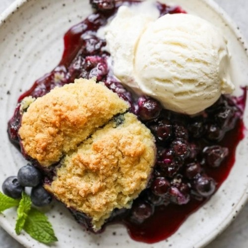 Overhead view of gluten free blueberry cobbler on a speckled plate with a side of vanilla ice cream.