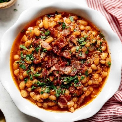 Overhead view of Instant Pot Baked Beans in a white bowl topped with bacon, parsley, and black pepper