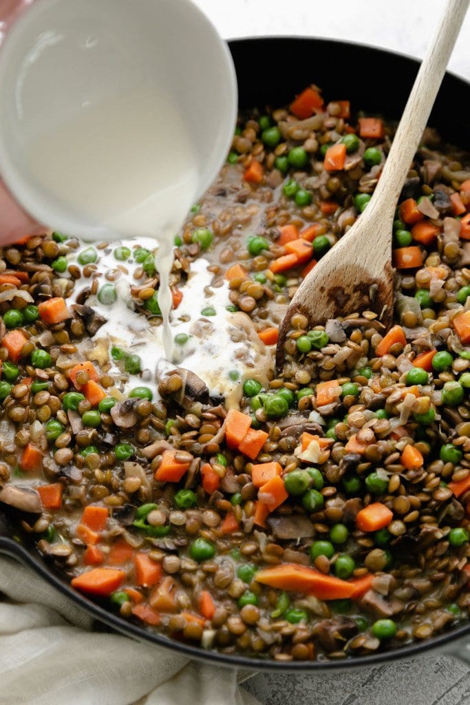 Lentil shepherd's pie filling in a cast iron skillet with a cornstarch slurry being poured into the skillet as a thickener.