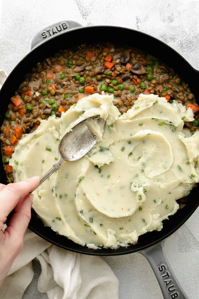 Creamy mashed potatoes being spread over a lentil-gravy filling for lentil shepherd's pie