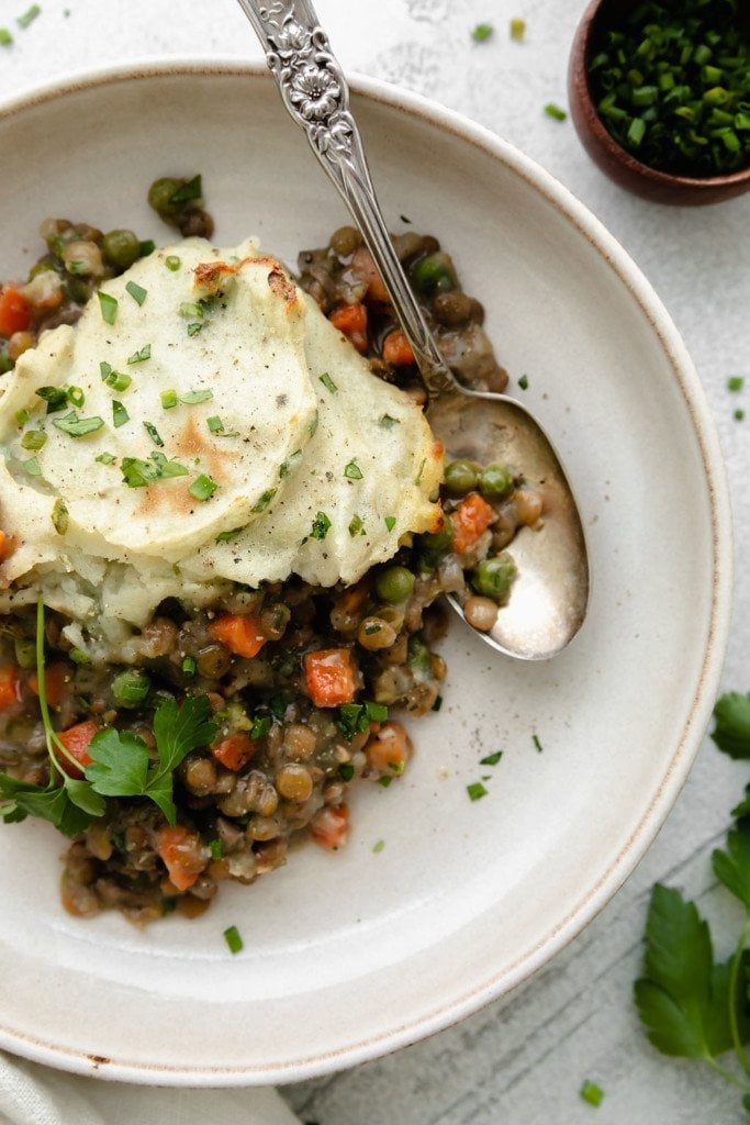 Overhead view of lentil shepherd's pie on a plate topped with baked mashed potatoes and fresh herbs.