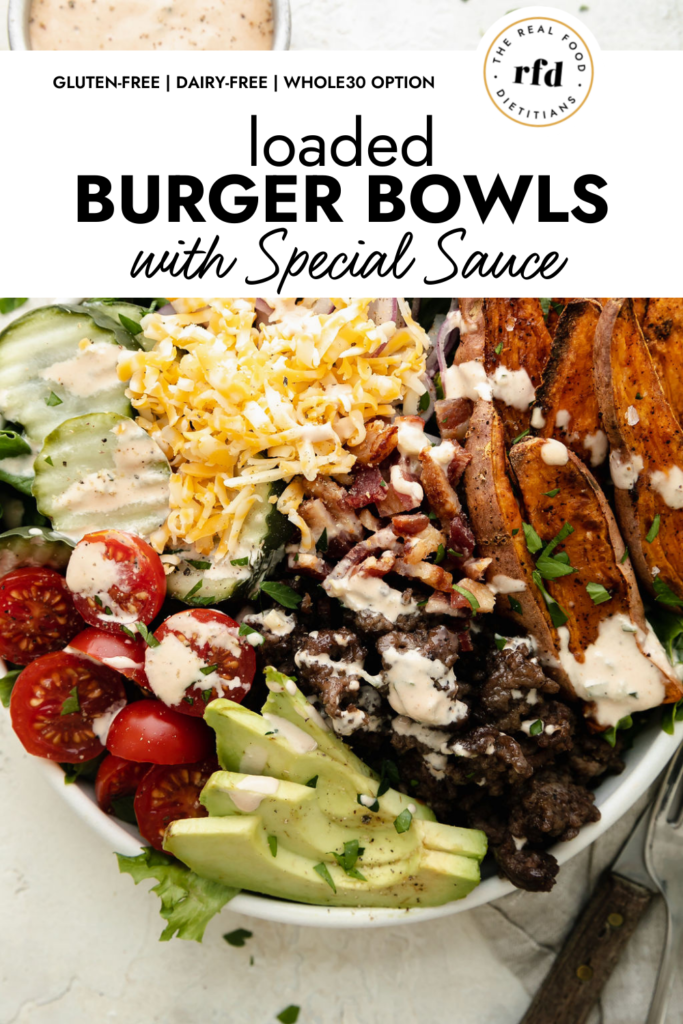 Overhead view of loaded burger bowl filled with lettuce, hamburger, sweet potato fries, pickles, cherry tomatoes, and shredded cheese and drizzled with special sauce. 