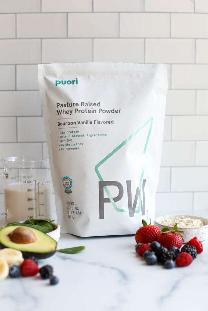 A bag of Puori whey protein powder against a white background with fresh fruit in the forefront. 