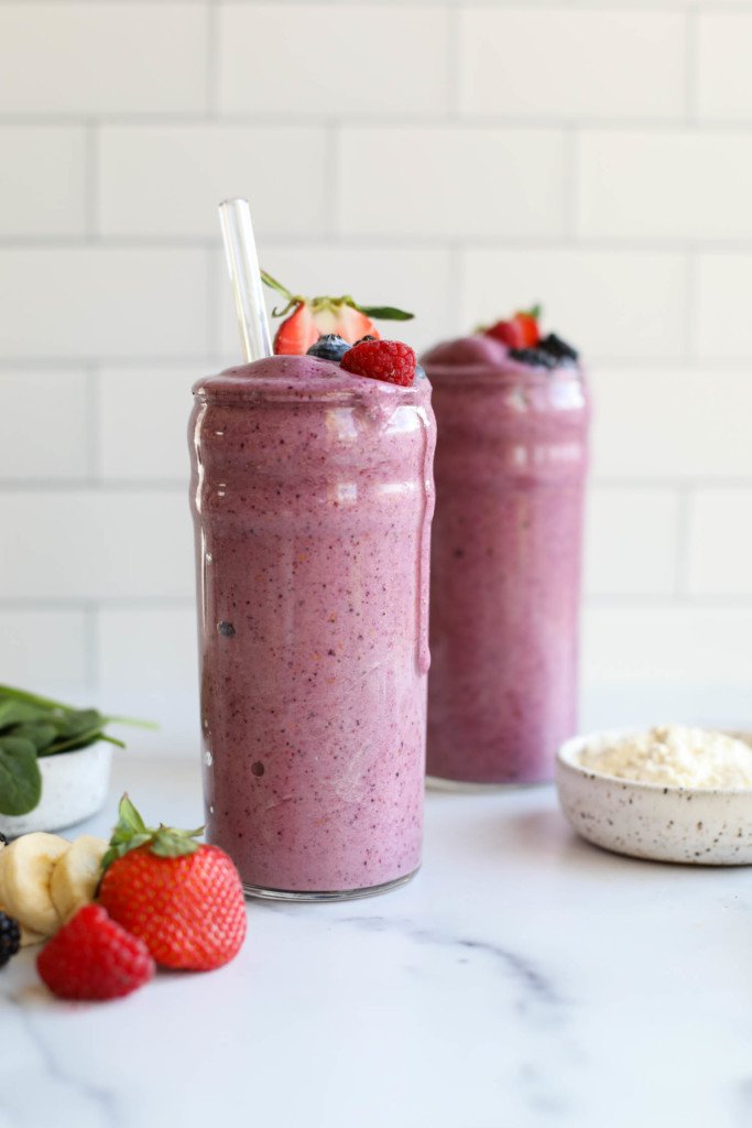 Two tall glasses of berry smoothie topped with fresh fruit for a plant-based protein powder review. 