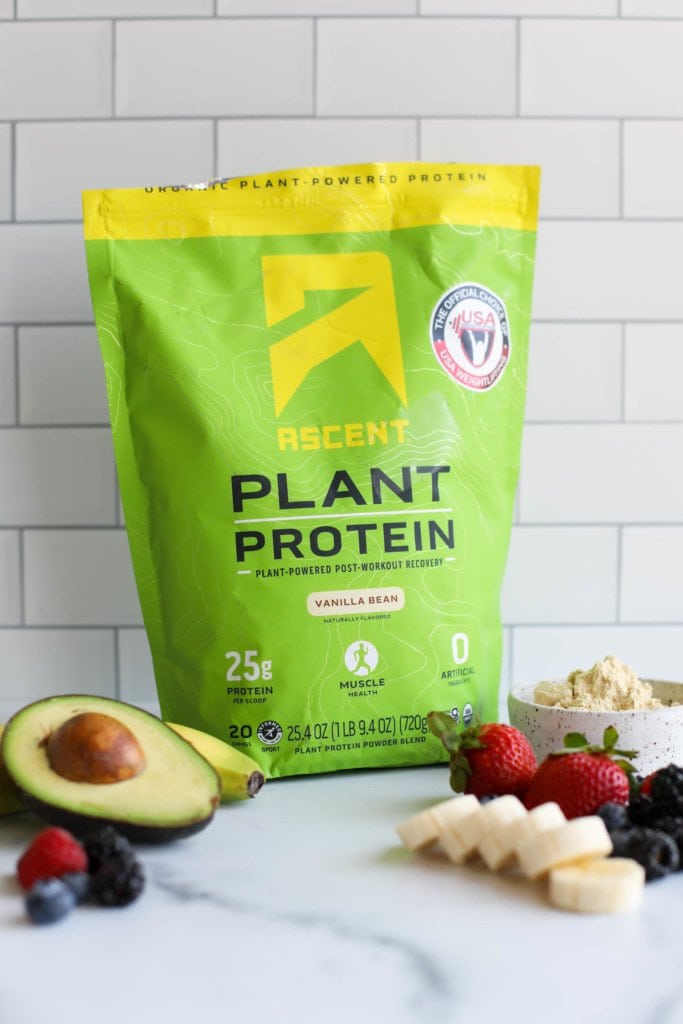 A green and yellow bag of Ascent plant based protein powder against a subway tiled background.