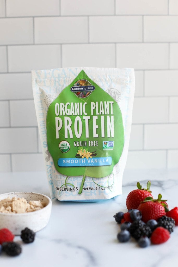 A package of Garden of Life Organic Plant Protein on a counter against a subway tile background with fresh berries in the forefront. 