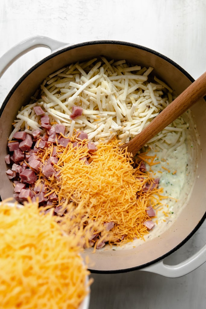 Overhead view of ingredients being stirred together in a baking dish for cheesy scalloped potatoes. 