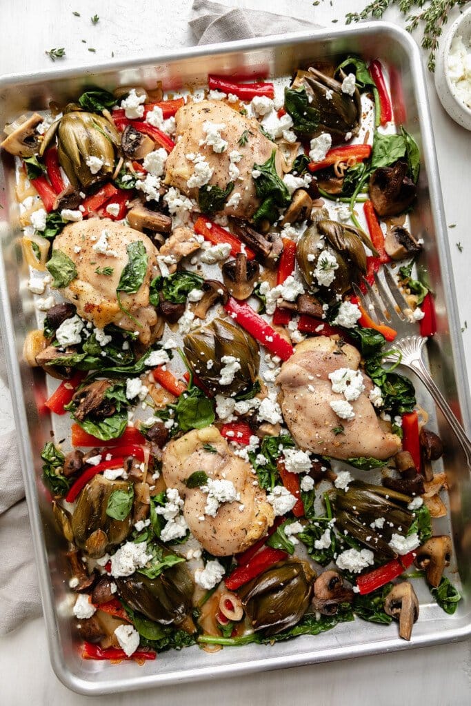 Sheet Pan Artichoke Chicken bake fresh from the oven on a deep silver baking sheet sprinkled with goat cheese. 