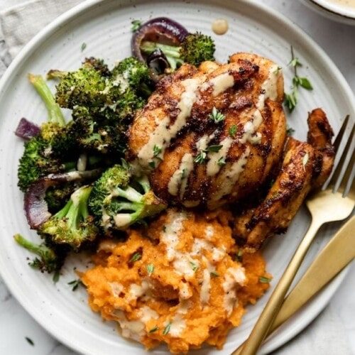 Overhead view of sheet pan chipotle chicken thighs with broccoli served on a white plate with a side of mashed sweet potatoes.