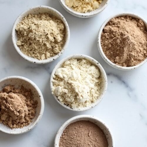 Overhead view of several small bowls filled with whey protein powders.