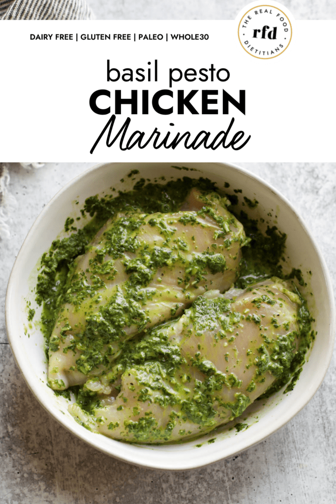 Overhead view of basil pesto chicken marinade in a white bowl with two chicken breasts. 