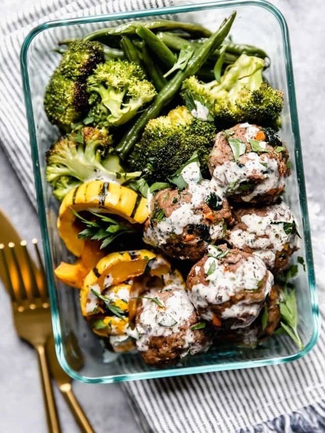 Overhead view of ultimate meal prep meatballs in a glass container with squash and broccoli, drizzled with ranch for a meal prep round up.