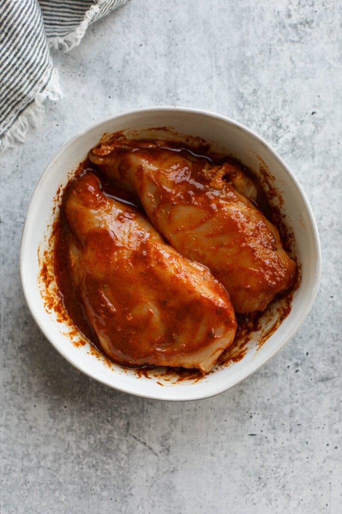 Two chicken breasts in white bowl with chicken fajita marinade.