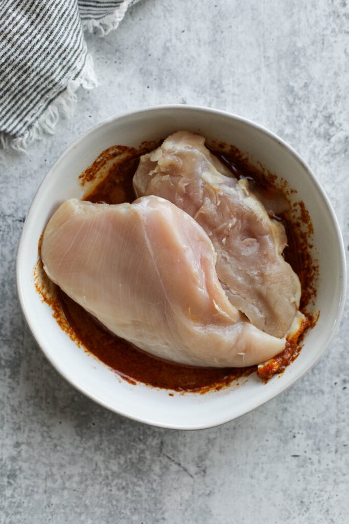Two chicken breasts in a white bowl with chicken fajita marinade.