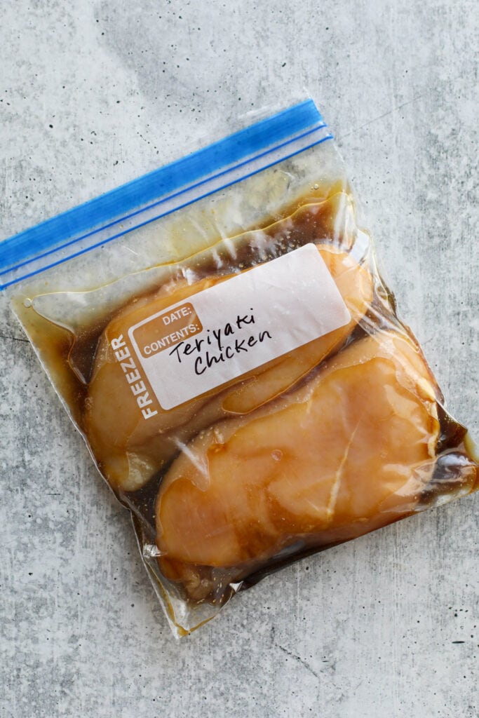 A ziplock bag filled with chicken breasts and teriyaki chicken marinade laying on a cement colored counter. 
