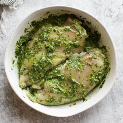 Overhead view of basil pesto chicken marinade in a white bowl.